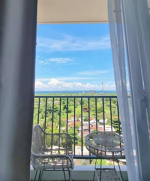 A balcony with two wicker chairs, a view of a green landscape, and a clear sky. - Oceanview Escape Steps to Shore Private Balcony (Lapu-Lapu)
