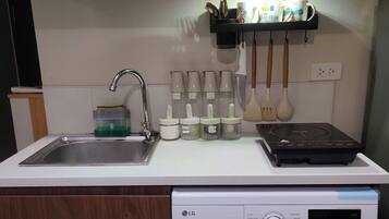 A compact kitchen with a built-in washing machine, a sink, and a shelf with kitchen utensils.