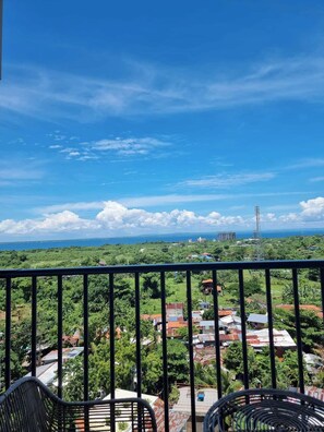 Un balcón con vista a un paisaje costero, que incluye edificios y una torre de transmisión.