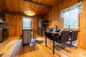 L’intérieur d’un chalet en bois comprend un coin repas, une cuisine et une grande fenêtre agrémentée de rideaux.