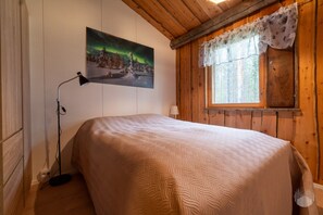 Une pièce avec un lit, une fenêtre avec un rideau, un tableau représentant les aurores boréales et une lampe.