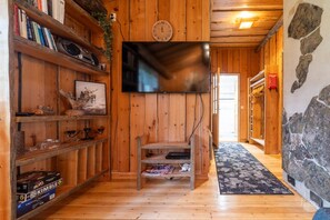 A wooden interior with a flat-screen TV mounted on the wall, a wooden staircase, and a stone wall. - Villa Pönttölä by Holiday in Lapland (Ruka)