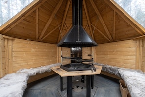 A wooden cabin with a central fireplace, a sloped roof, and a fur-lined bench. - Villa Pönttölä by Holiday in Lapland (Ruka)