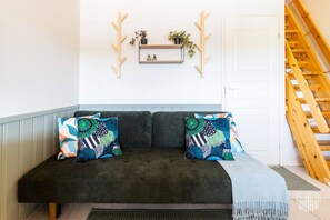 A dark green sofa with patterned cushions, a small shelf with plants, and a wooden staircase. - Postintie 1617 by Holiday in Lapland (Levi)