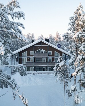 A large, multi-story building with a symmetrical facade, surrounded by snow-covered trees. - Leviraitti 14 B6 by Holiday in Lapland (Levi)