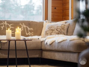 A cozy living room with a beige sofa, two lit candles on a small table, and a fluffy throw blanket.