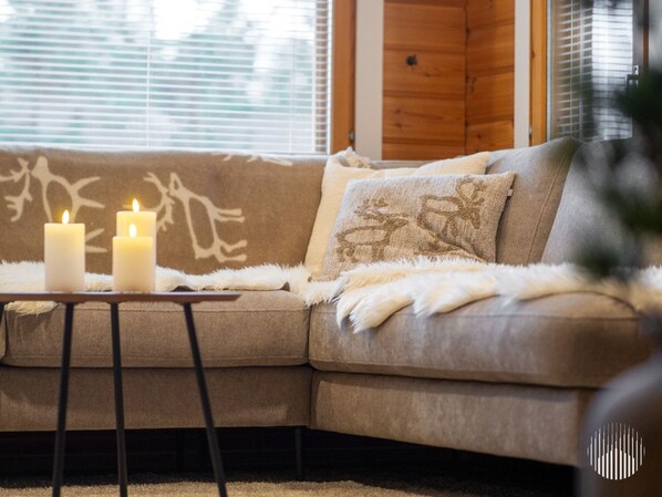 A cozy living room with a beige sofa, two lit candles on a small table, and a fluffy throw blanket.