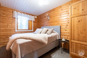 Ein gemütliches Zimmer mit einem Bett, einem Vorhangfenster, einem Wandbild eines Reh-Kopfes und einem kleinen Tisch mit einer Lampe.