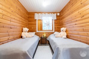 Una habitación tipo cabaña con dos camas, paredes de madera, un ventanal con decoración de estrella y una pequeña mesa con lámpara.