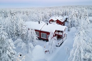 Eine zweistöckige rote Holzhütte, umgeben von schneebedeckten Bäumen.