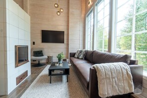 Ein modernes Wohnzimmer mit großem Fenster, Flachbildfernseher, braunem Ledersofa und Couchtisch.