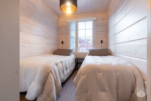Ein Zimmer mit zwei Betten, Holzwänden, einem Fenster und einer Lampe.