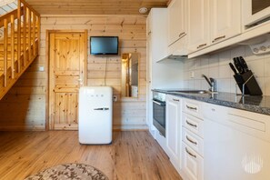 A compact kitchen with wooden walls, a built-in TV, white cabinets, and a refrigerator.