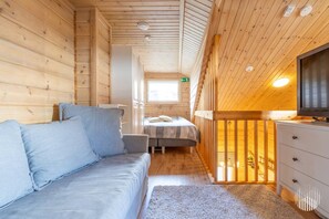 A cabin interior with a sofa, a bed, a TV, and a wooden ceiling.