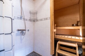 A shower area with a tiled wall, a showerhead, and a wooden bench.
