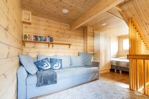 A wooden interior with a sofa, pillows, a bookshelf, and a staircase.