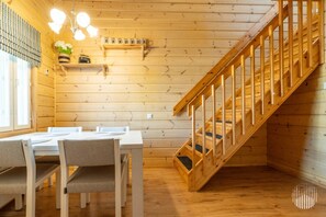 A wooden interior with a dining table, chairs, a staircase, and a shelf with mugs.