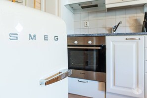 A kitchen with a white refrigerator labeled 'SMEG,' stainless steel oven, white cabinets, and a granite countertop.