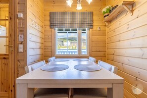A wooden-paneled room with a large table and chairs, a window with a view, and a plaid curtain.