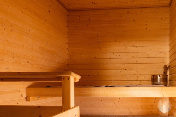 A wooden sauna room with benches and a metal container.