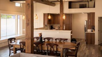 A modern kitchen with wooden cabinets, a dining area with a round table and chairs, and a living room with a sofa.