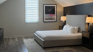 A bedroom with a bed, a window with blinds, a ceiling fan, and a nightstand with a lamp.