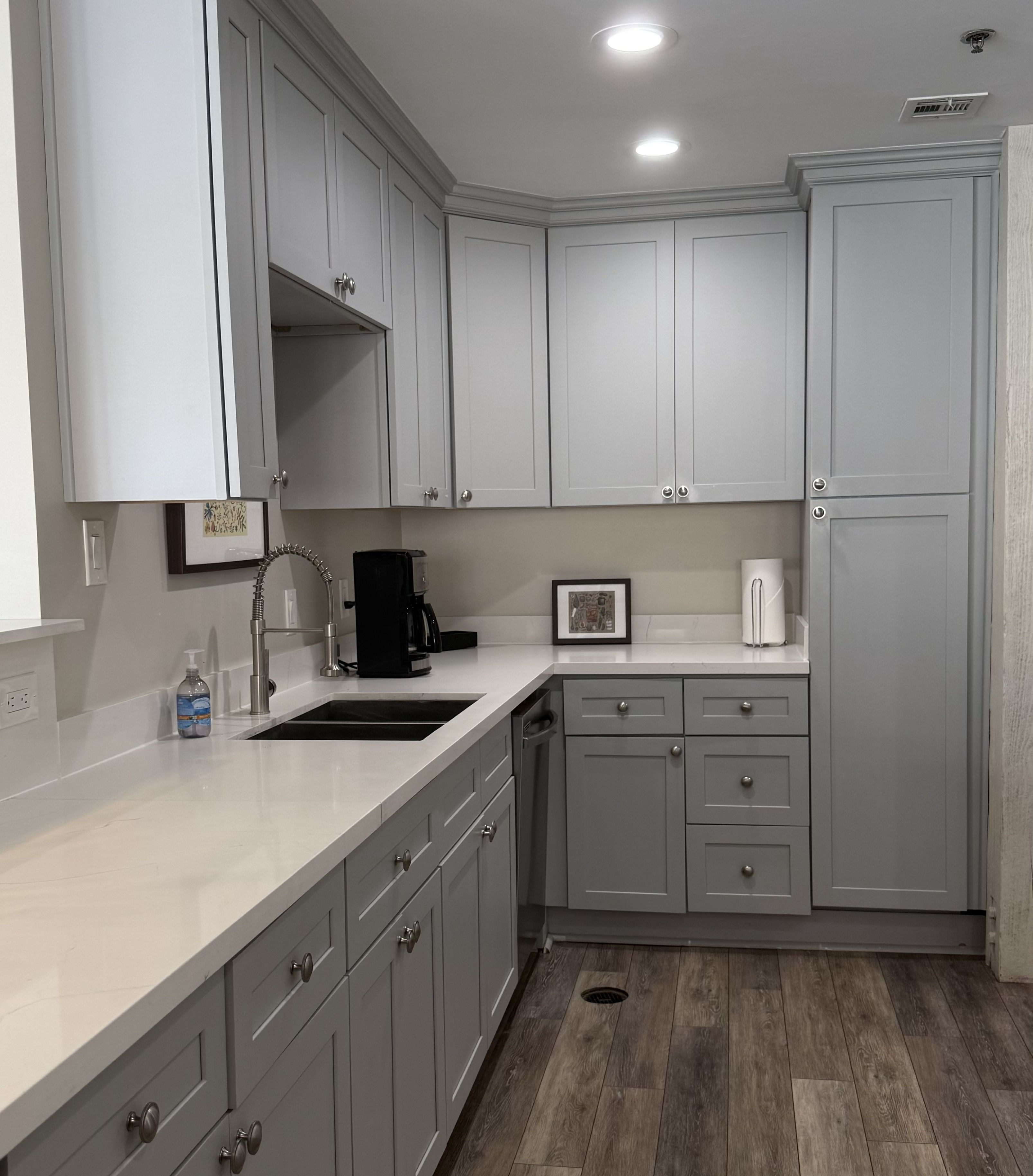 A kitchen with grey cabinets, a sink, a coffee maker, and a refrigerator.