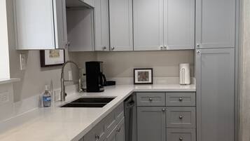 A kitchen with grey cabinets, a sink, a coffee maker, and a refrigerator.