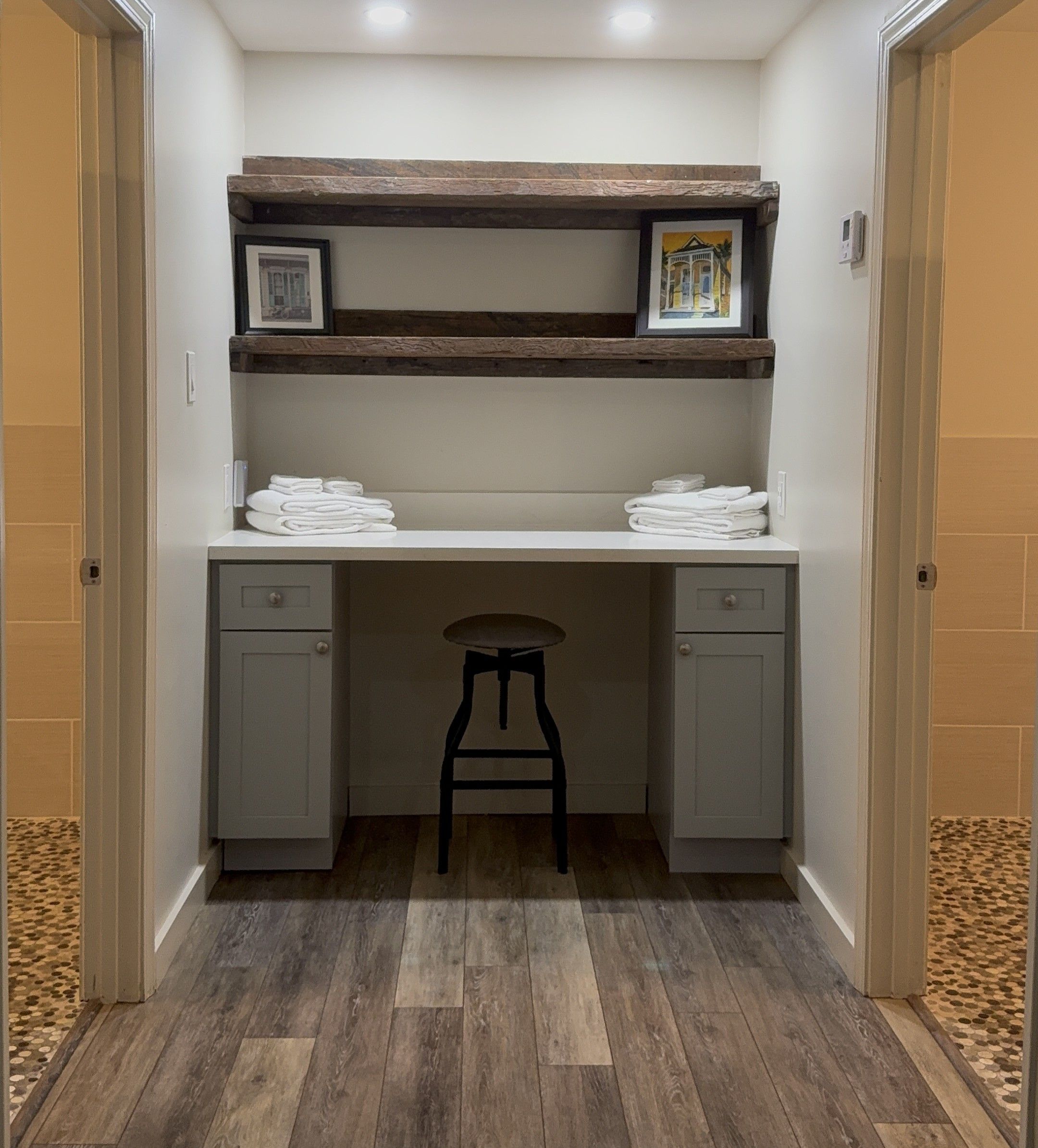 A small, enclosed room with a desk, two drawers, a stool, and a shelf with towels.