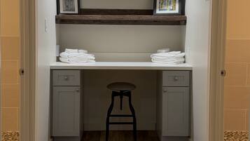 A small, enclosed room with a desk, two drawers, a stool, and a shelf with towels.