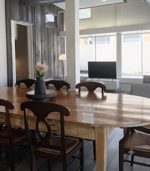 Een eetruimte met een houten tafel, stoelen, een vaas met bloemen en een televisie op de achtergrond.