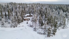 Eine Blockhütte, umgeben von dichtem Wald, in einer verschneiten Landschaft.