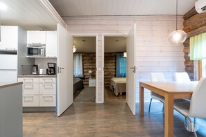 A modern kitchen with white cabinets and a dining area with a wooden table and chairs. - Villa Quality side B by Holiday in Lapland (Ruka)