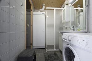 A compact bathroom with a washing machine, a glass shower enclosure, and a small step stool. - Iso-Ylläksentie 42 B 2507 by Holiday in Lapland (Ylläs)