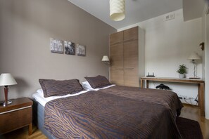 A bedroom with a bed, bedside tables, a desk, a wardrobe, and wall art.