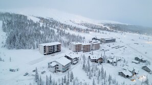 Estância coberta de neve com vários edifícios, incluindo um hotel com vários andares e uma pousada com um telhado imponente.