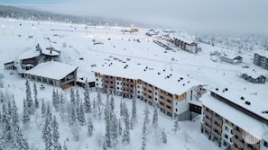 Un complejo turístico nevado con varias construcciones, incluyendo un hotel con balcones y un estacionamiento.