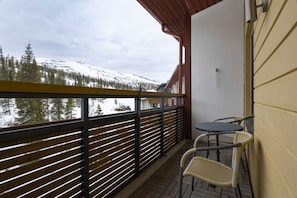 Un balcón con vista a una montaña nevada, una mesa con sillas y una barandilla de madera.