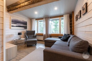 L’intérieur d’un chalet chaleureux, avec un canapé, un fauteuil et une petite table sur laquelle se trouve une lampe.