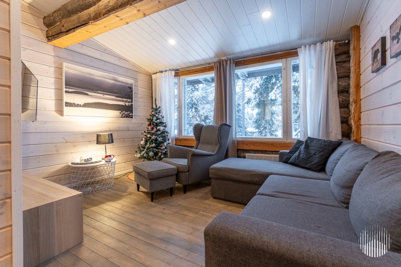 Un salon chaleureux avec un plancher en bois, un canapé gris, une petite table avec une lampe et un sapin de Noël.