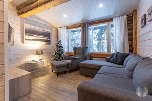 Un salon chaleureux avec un plancher en bois, un canapé gris, une petite table avec une lampe et un sapin de Noël.