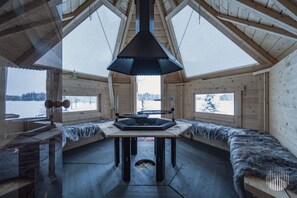 Una cabana de fusta amb una llar de foc central, grans finestres i vistes a un paisatge cobert de neu.