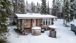 A log cabin with a snow-covered roof, a hot tub, and a wooden deck. - Villa Quality side A by Holiday in Lapland (Ruka)