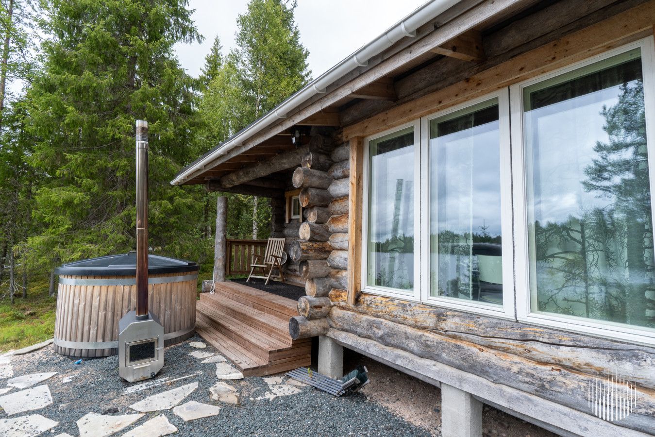 A log cabin with a porch, a hot tub, and a stone pathway.