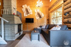 A log cabin interior with a stone fireplace, a gray sofa, and two mounted animal hides.