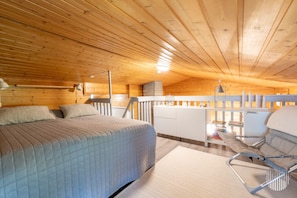Une cabane confortable avec un lit, une chaise, une petite kitchenette et un plafond en bois.
