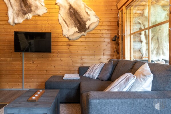 A cozy living room with a sectional sofa, a flat-screen TV, and a large window. - HilleVilla by Holiday in Lapland (Ylläs)