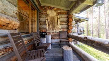 Une cabane en rondins dotée d’un porche avec des bancs en bois et un tapis en fourrure.