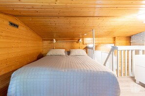 Une chambre dans une cabane en bois, avec un lit, deux lampes de chevet et une rambarde blanche.