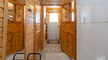 Un couloir en bois avec un banc, une porte ornée d’un motif en forme de cœur et un paillasson avec l’inscription « HOME » au bout.